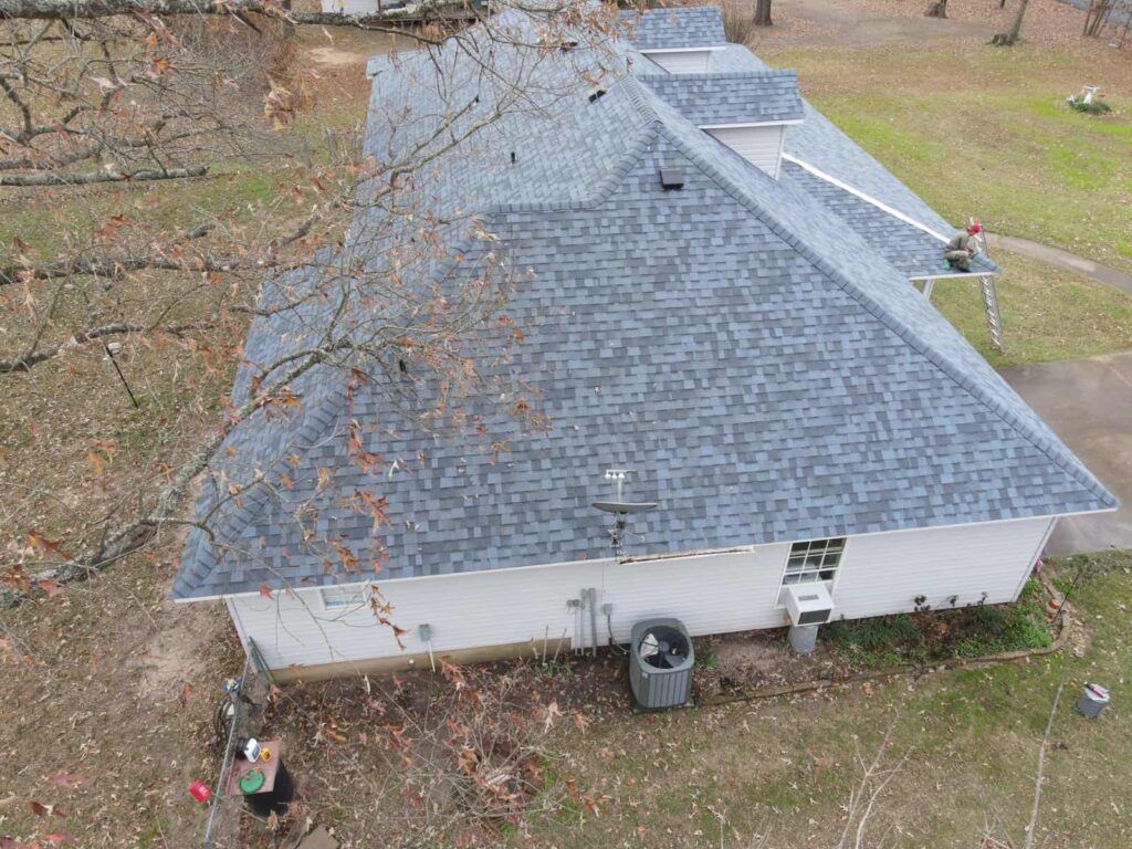 Fallen limbs and storm debris around a home with a light grey shingle roof