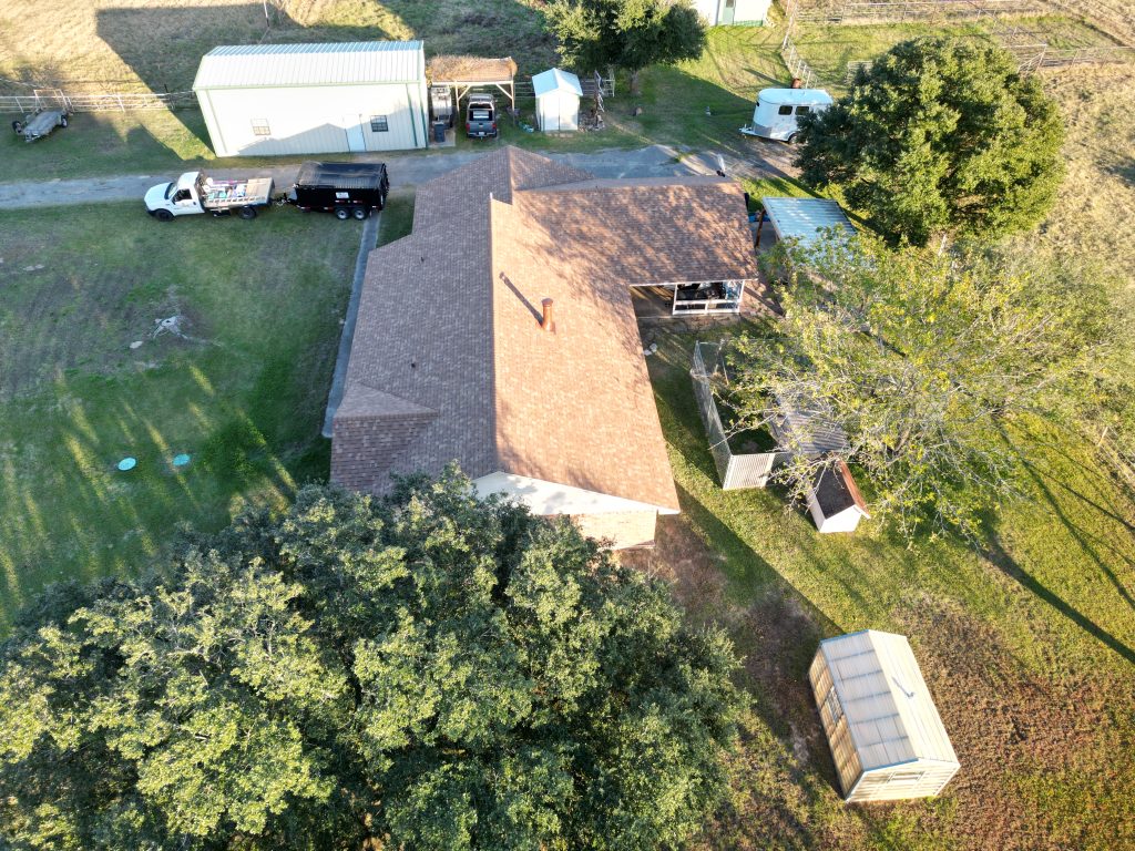 Aerial view of a tan shingle roof on a long ranch house among trees