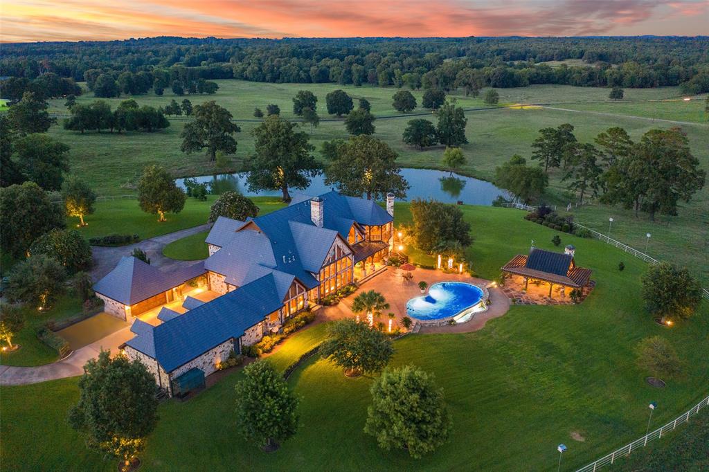 Dusk aerial of a large lakeside home with a metal roof and a pool