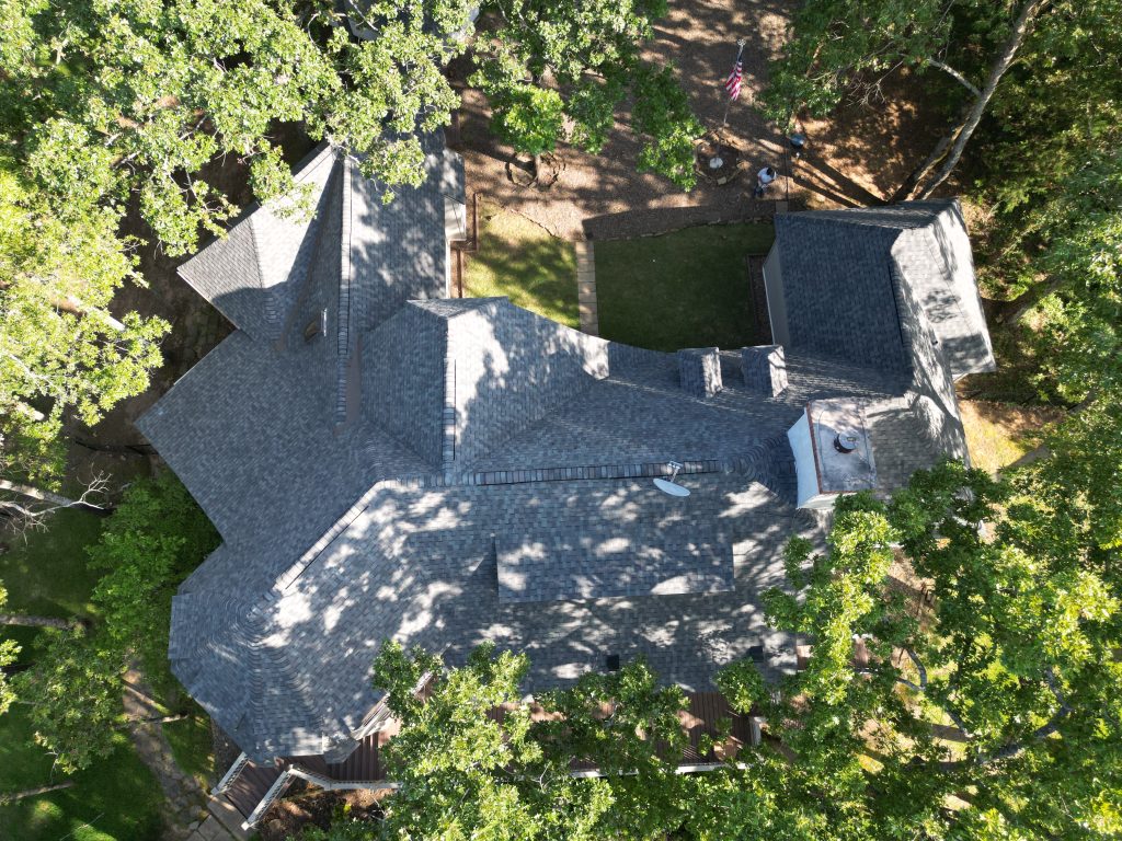 Roof Inspection in Emory, TX 7 Aerial view of a large gray shingle roof with multiple gables, surrounded by mature trees