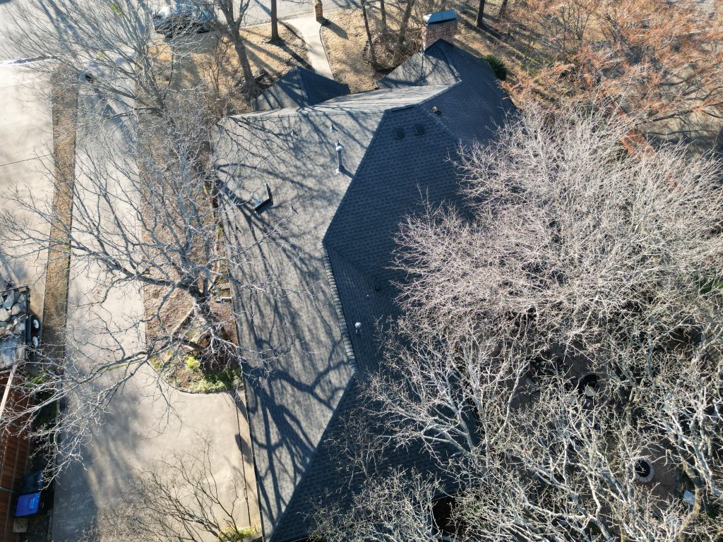 Aerial of a finished shingle roof among bare trees in Greenville, Texas